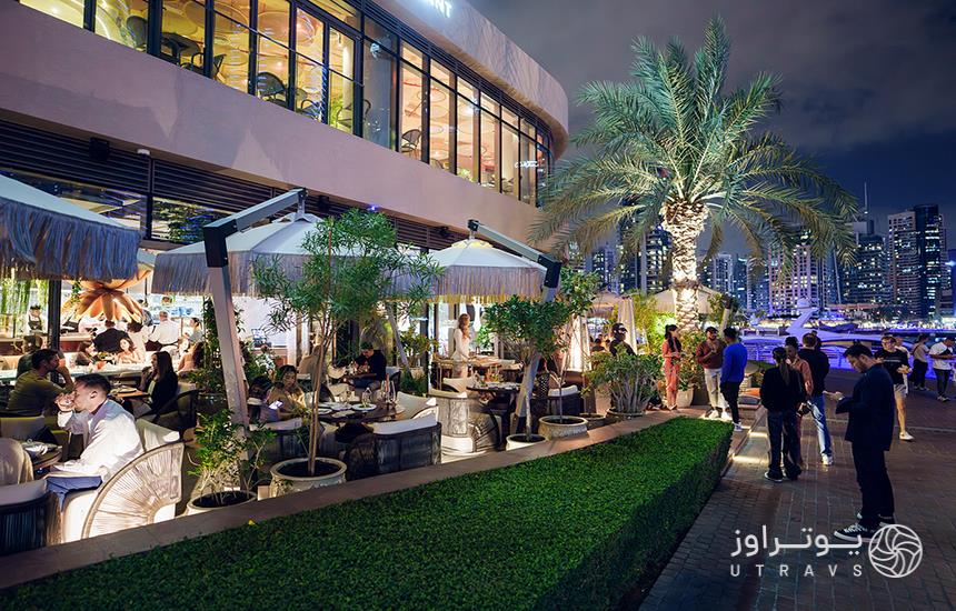 تصویری از یک رستوران در فضای باز در مارینا مال دبی که فضاهای آلاچیق‌مانند دارد و جمعیت در آن دیده می‌شود.